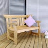 Natural wood outdoor garden bench with purple cushion on a wooden deck with potted flowers and slatted wall.