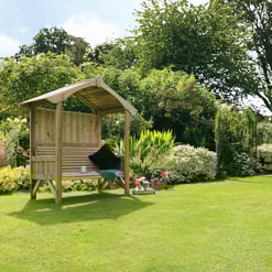 Light wood garden swing with roof on lush green lawn surrounded by flowering plants and trees, perfect outdoor furniture for relaxation and enjoying garden beauty.