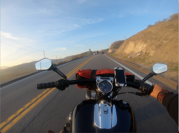 In first person, Karif Battle, founder of Theoretical Fiends LLC, is riding his Harley Davidson motorcycle with one hand through the canyon.