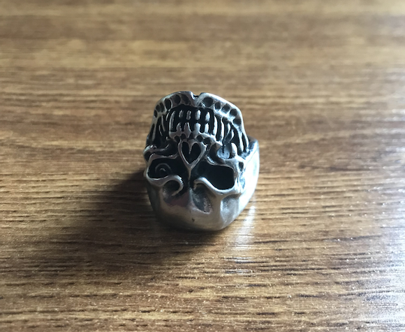 Karif Battle, founder of Theoretical Fiends LLC, took a picture of his biker ring. A terminator skull ring rests upside down on a dusty wooden work desk.