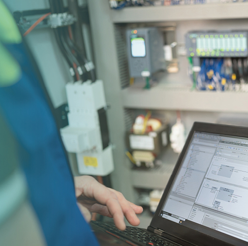 Programmer of PLC checks correct function of program in PLC with electrical cabinet in background