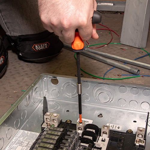 klein 33804 ProFlex Impact-Rated Interchangeable Ratcheting T-Handle Set with a person holding a screwdriver working on a load center