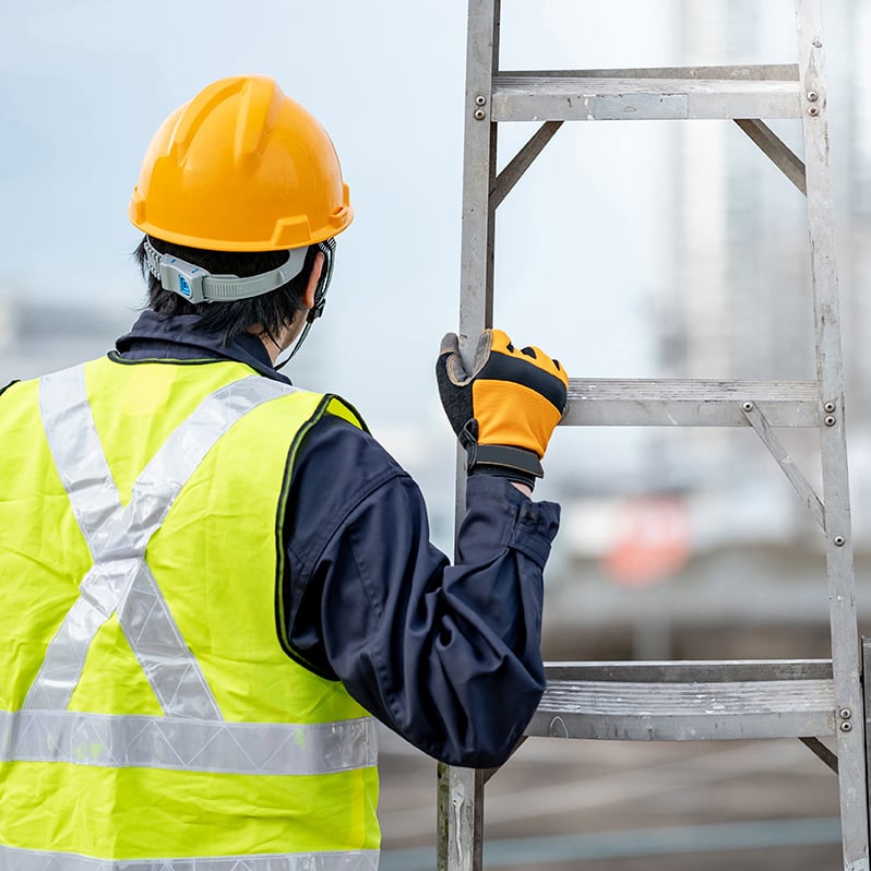 maintenance worker man with safety helmet and green vest carrying aluminium step ladder at construction site. Civil engineering, Architecture builder and building service concepts