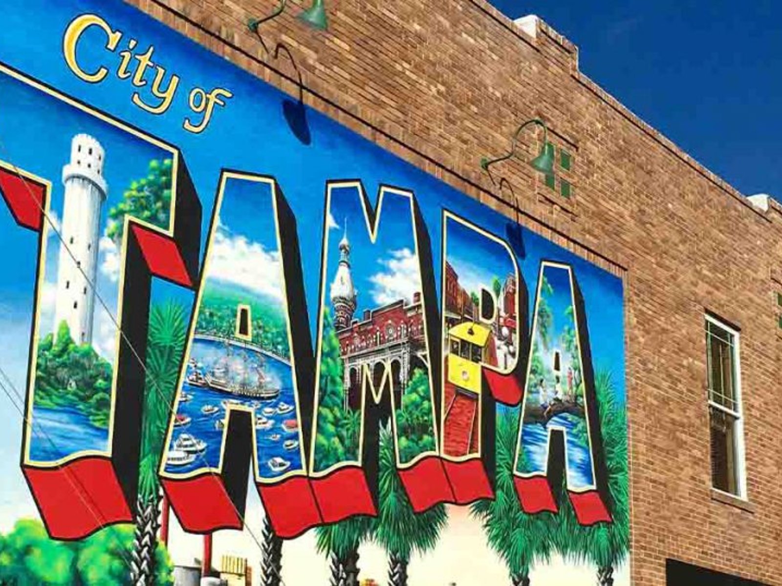 Colorful Tampa mural painted on a brick building, featuring city landmarks inside large block letters