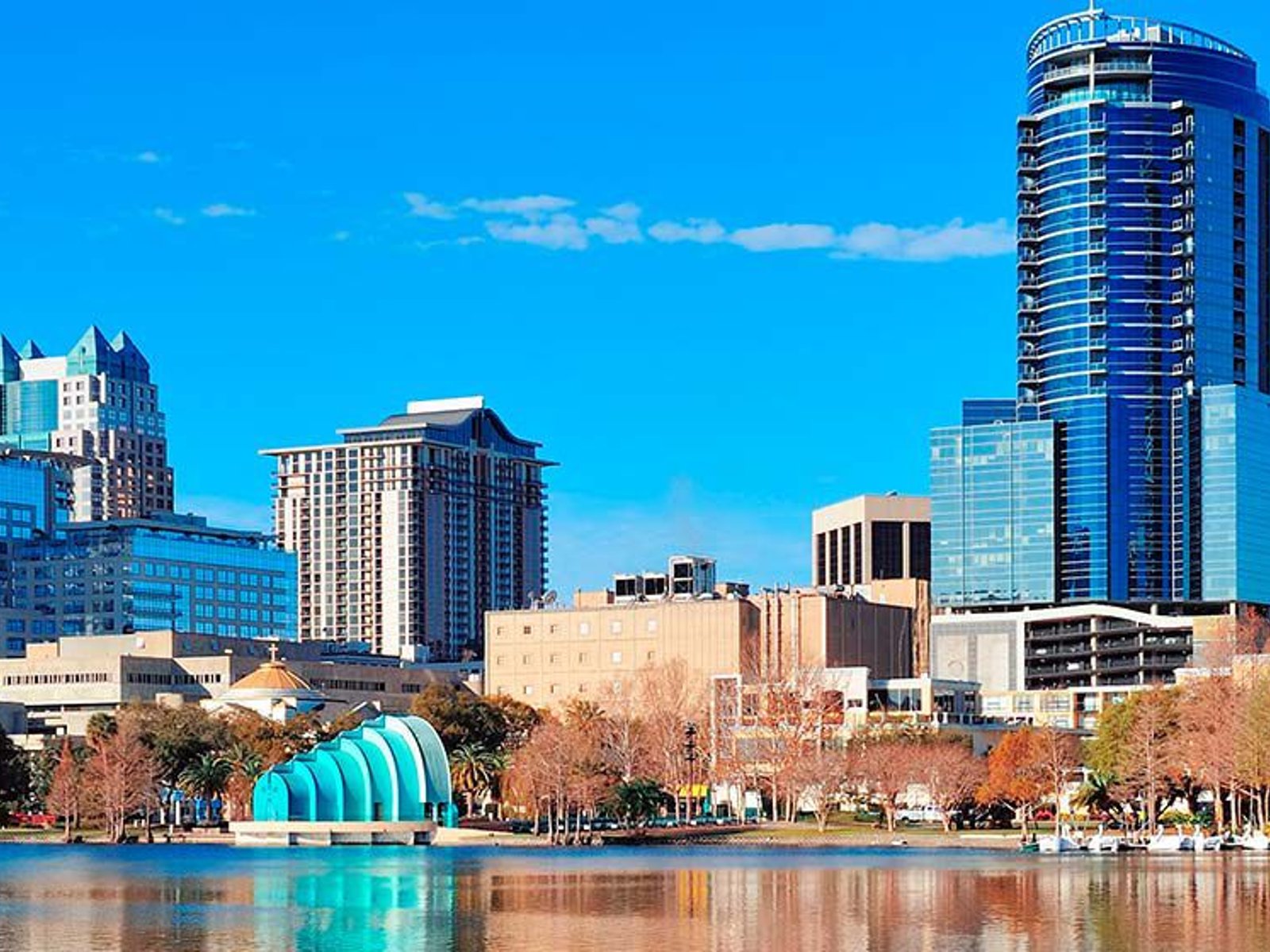Downtown Orlando skyline viewed across Lake Eola with high-rise buildings, palm trees, and the colorful Walt Disney Amphitheater.