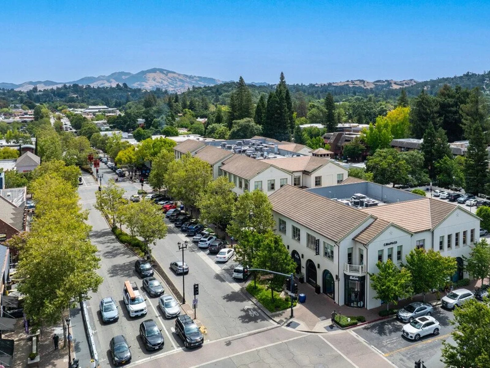 Aerial view of downtown Lafayette, California, with tree-lined streets, commercial buildings, neighborhoods, and hills in the background.