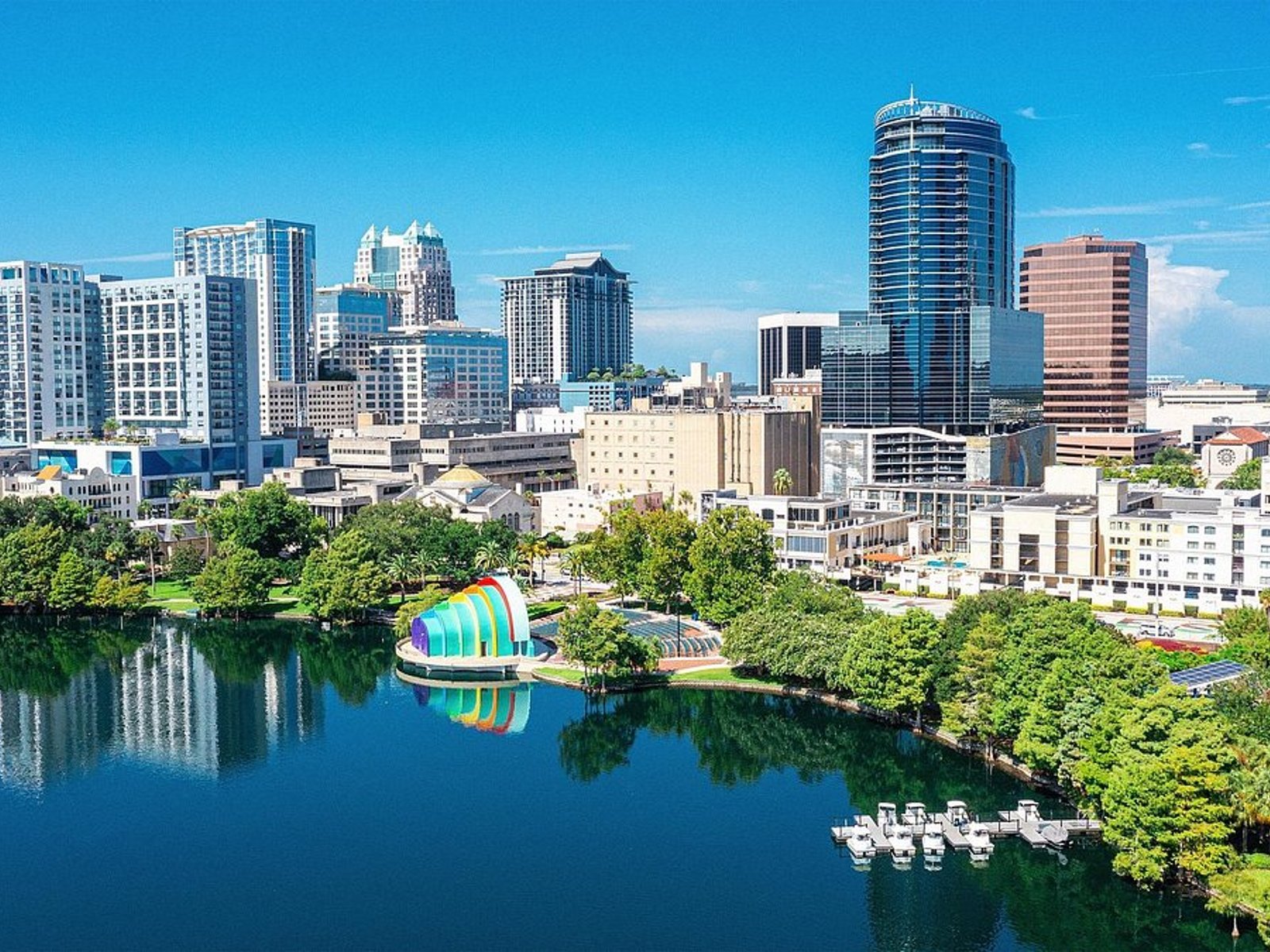 Downtown Orlando skyline viewed across Lake Eola with high-rise buildings, palm trees, and the colorful Walt Disney Amphitheater.