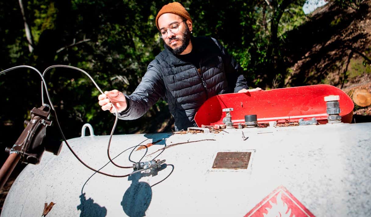 Joan Lora revisa un tanque de propano perjudicado por un árbol caído durante las tormentas de invierno de 2023 en California del Norte. El árbol debería haber sido retirado por PG&E, pero nunca lo hizo. Foto por Brooke Anderson.