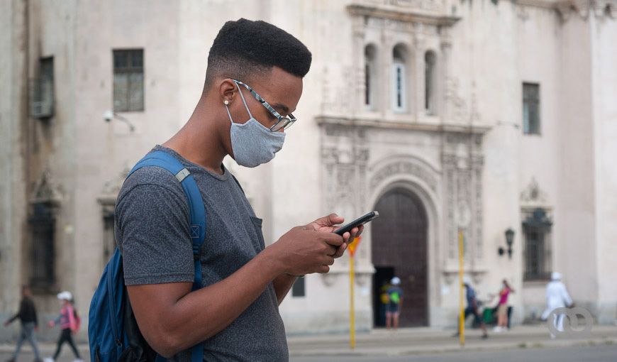 Hombre con nasobuco mira su celular en la calle. Cuba