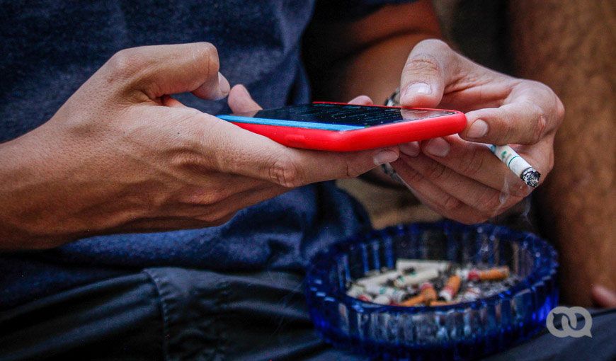 Hombre cubano sostiene un teléfono celular mientras fuma.