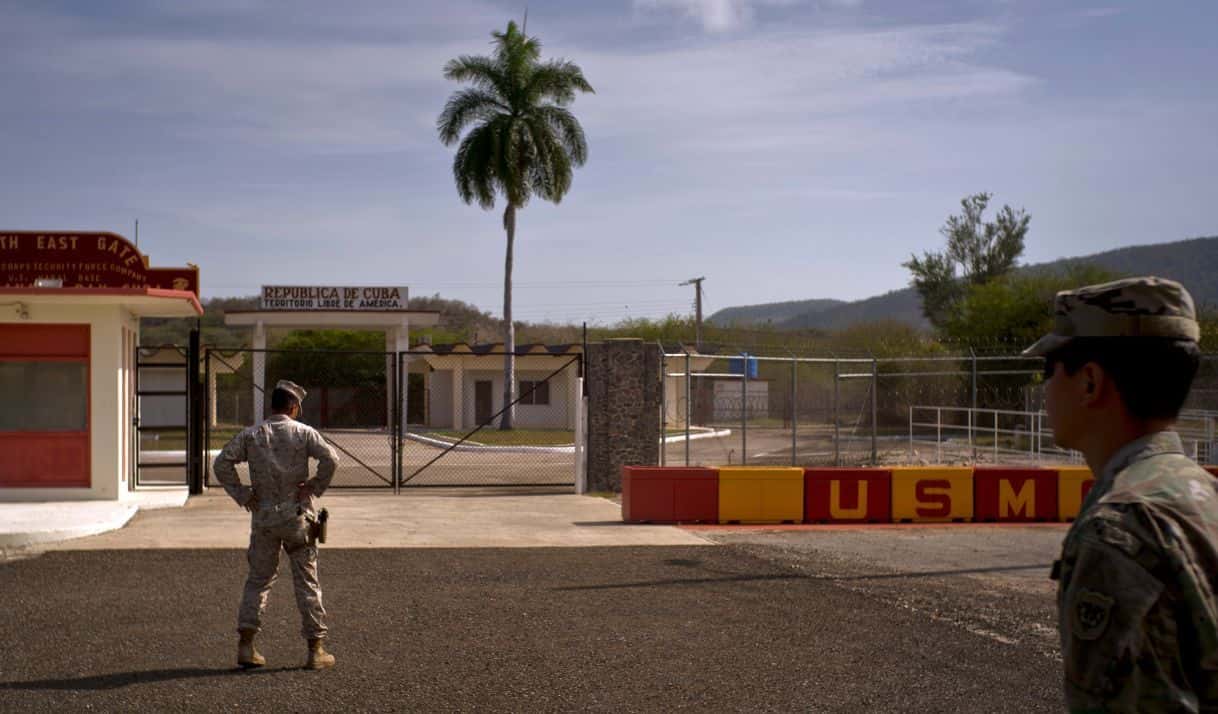 ARCHIVO - En esta fotografía revisada por oficiales militares de Estados Unidos, un soldado del ejército, derecha, y un miembro de la infantería de Marina permanecen frente a las verjas que separan el territorio cubano de la Base Naval estadounidense, el 6 de junio de 2018, en Bahía de Guantánamo, Cuba. (AP Foto/Ramón Espinosa, archivo)