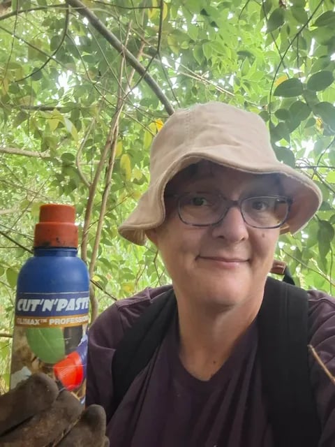A close-up portrait of a woman in a sun hat holding a bottle of weed gel in dense bush.