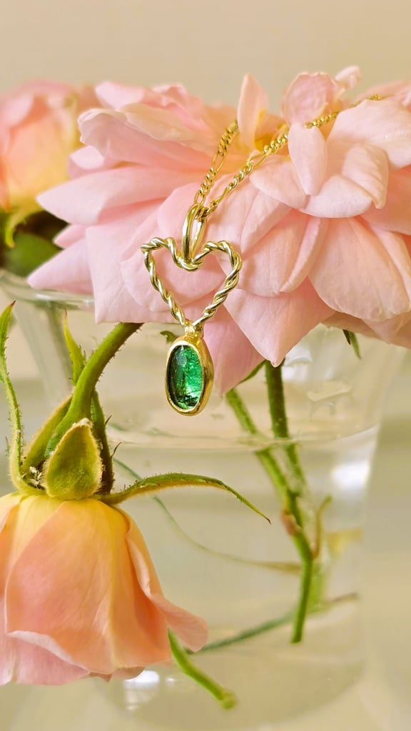 Emerald stone on a gold chain with flowers in the background