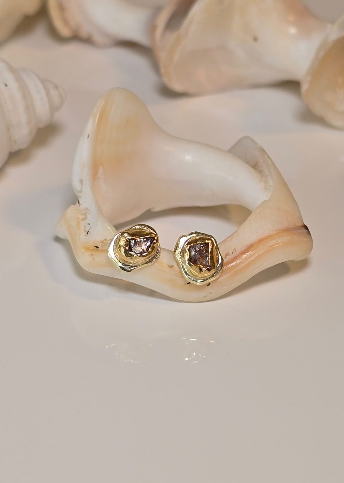 Raw Diamond Gold Stud Earrings resting on a shell