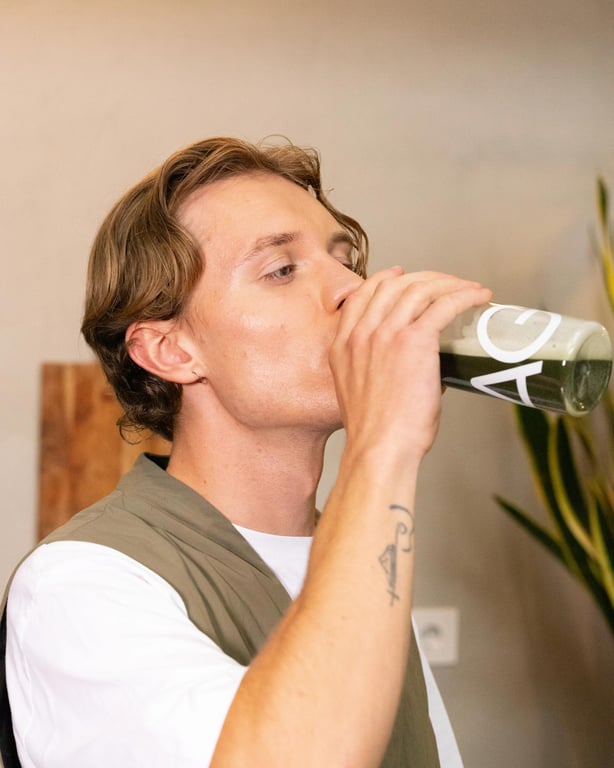 A man drinking AG1 from a glass bottle