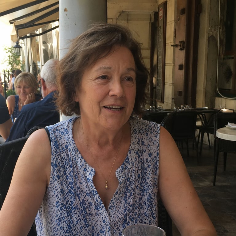 A woman in her late sixties at an outdoor cafe in a sleeveless blouse, arms relaxed