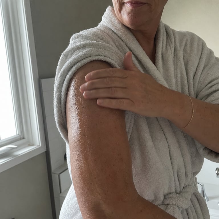 A woman's hand smoothing golden body oil onto her upper arm after a shower