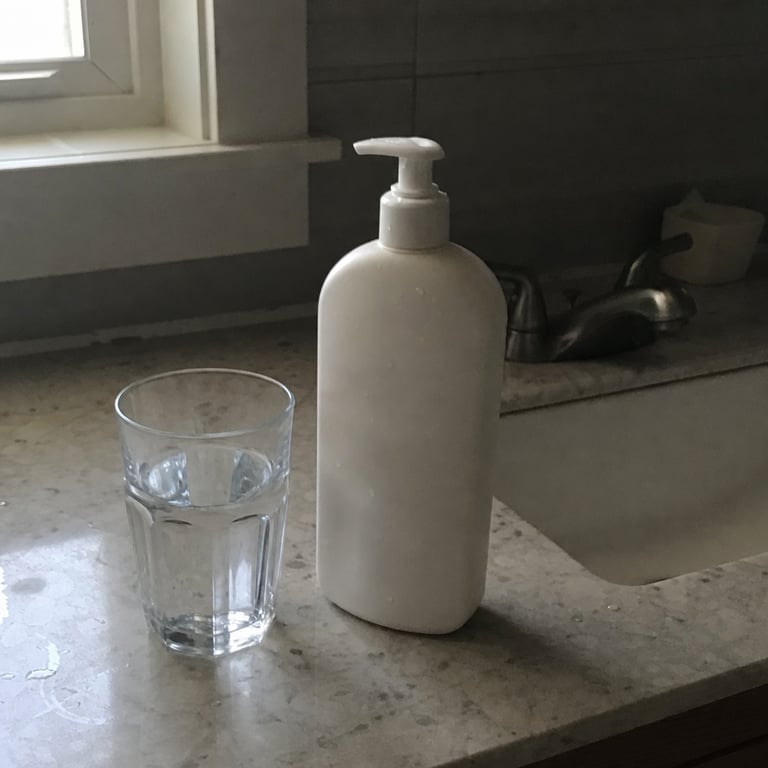 A generic white body-lotion bottle on a bathroom counter next to a clear glass of water