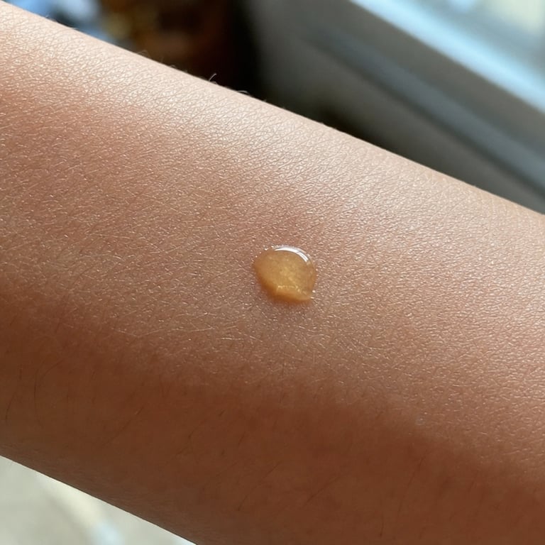 Extreme close-up of a droplet of golden oil absorbing into the texture of mature skin on a forearm