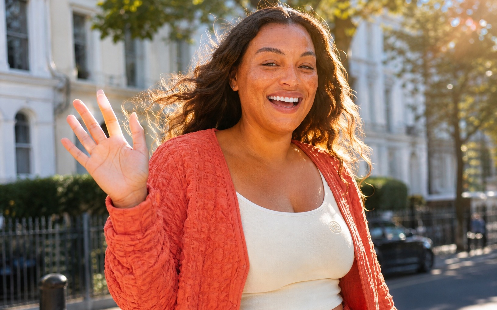 A woman waving on a sunny London street