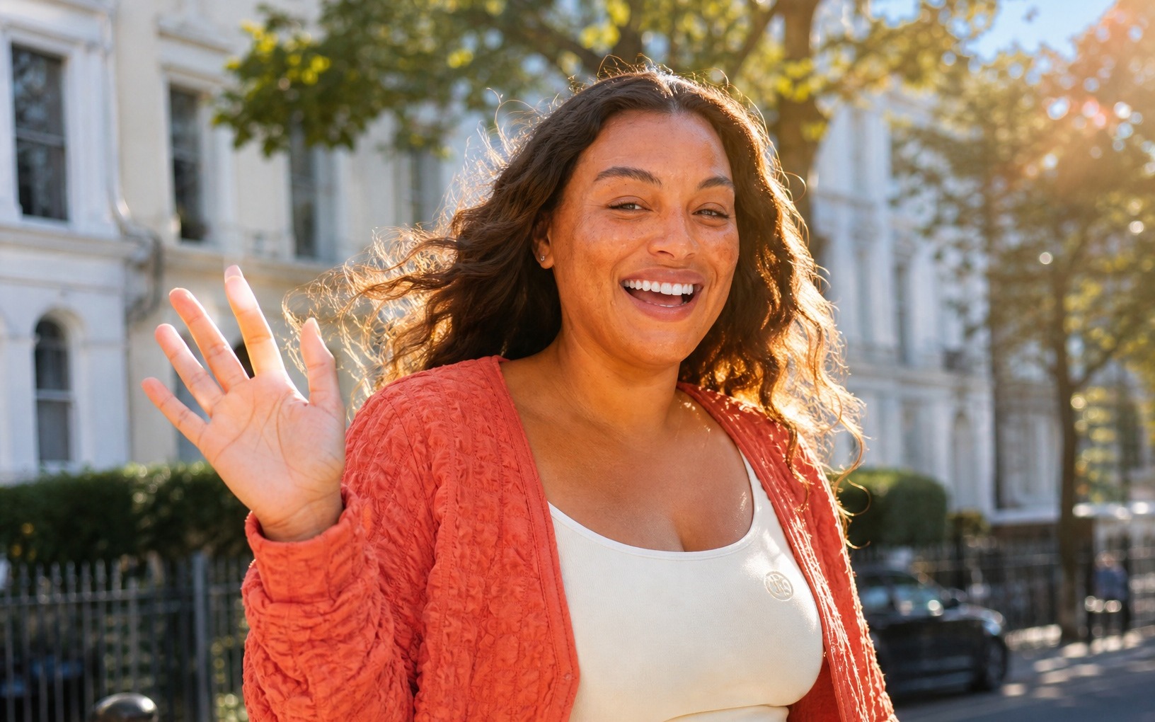 A woman waving on a sunny London street