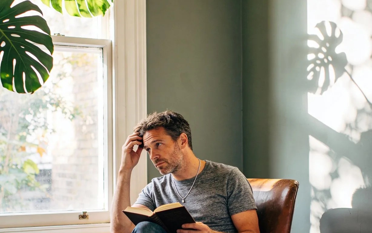 A man reading in an armchair by the window