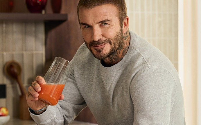 David Beckham at a kitchen counter with a glass of IM8 and the Daily Ultimate cartons