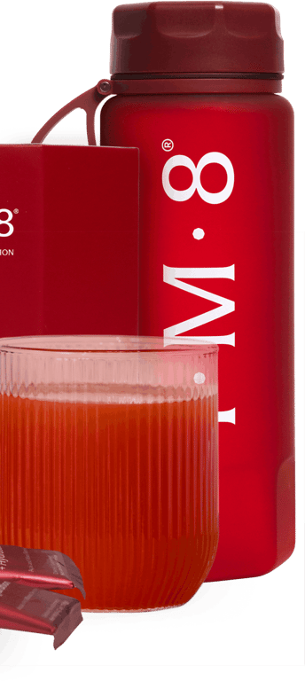 The IM8 signature red bottle beside a glass of mixed Daily Ultimate Essentials