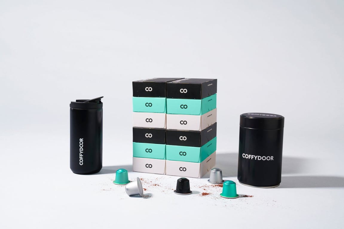 The Coffydoor Starter Kit: capsule boxes in black, mint and cream stacked between a matte black thermos mug and a storage tin