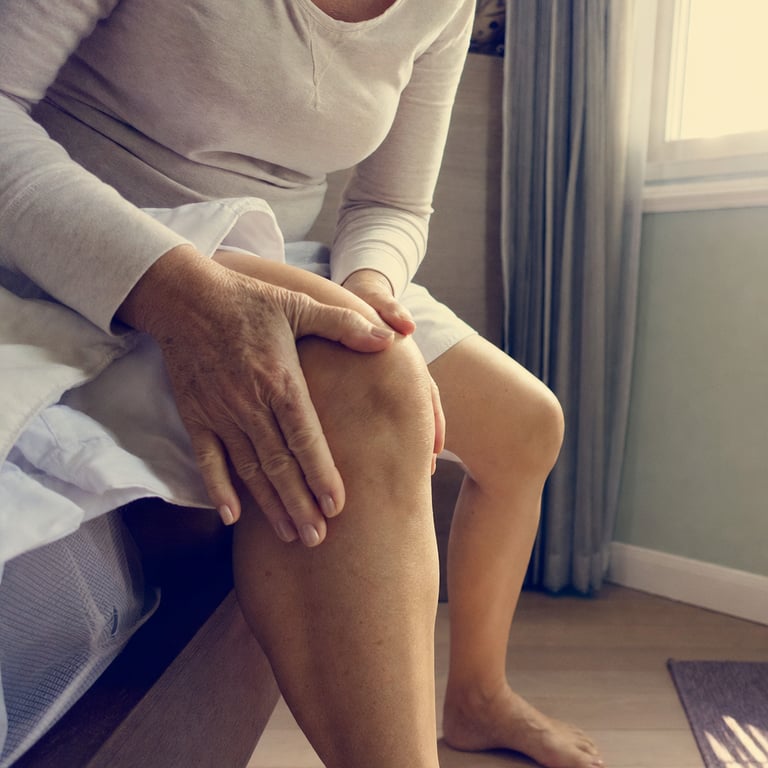 Close-up of an older person's hands resting on a stiff knee in early morning light