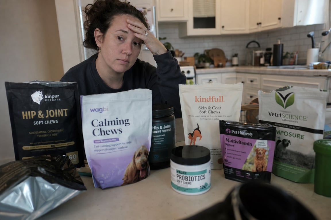Woman sitting at kitchen table surrounded by half-used dog supplement bottles, looking tired