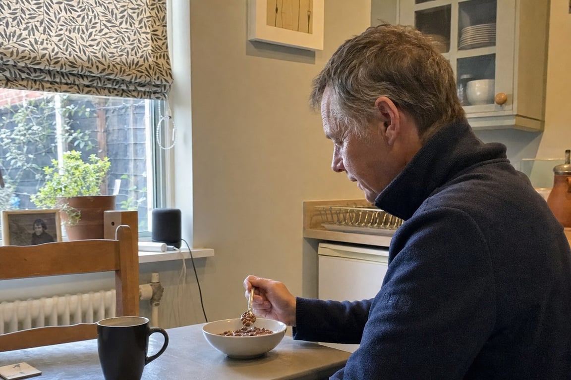 A man in his sixties eating a bowl of cereal at his kitchen table on an ordinary morning