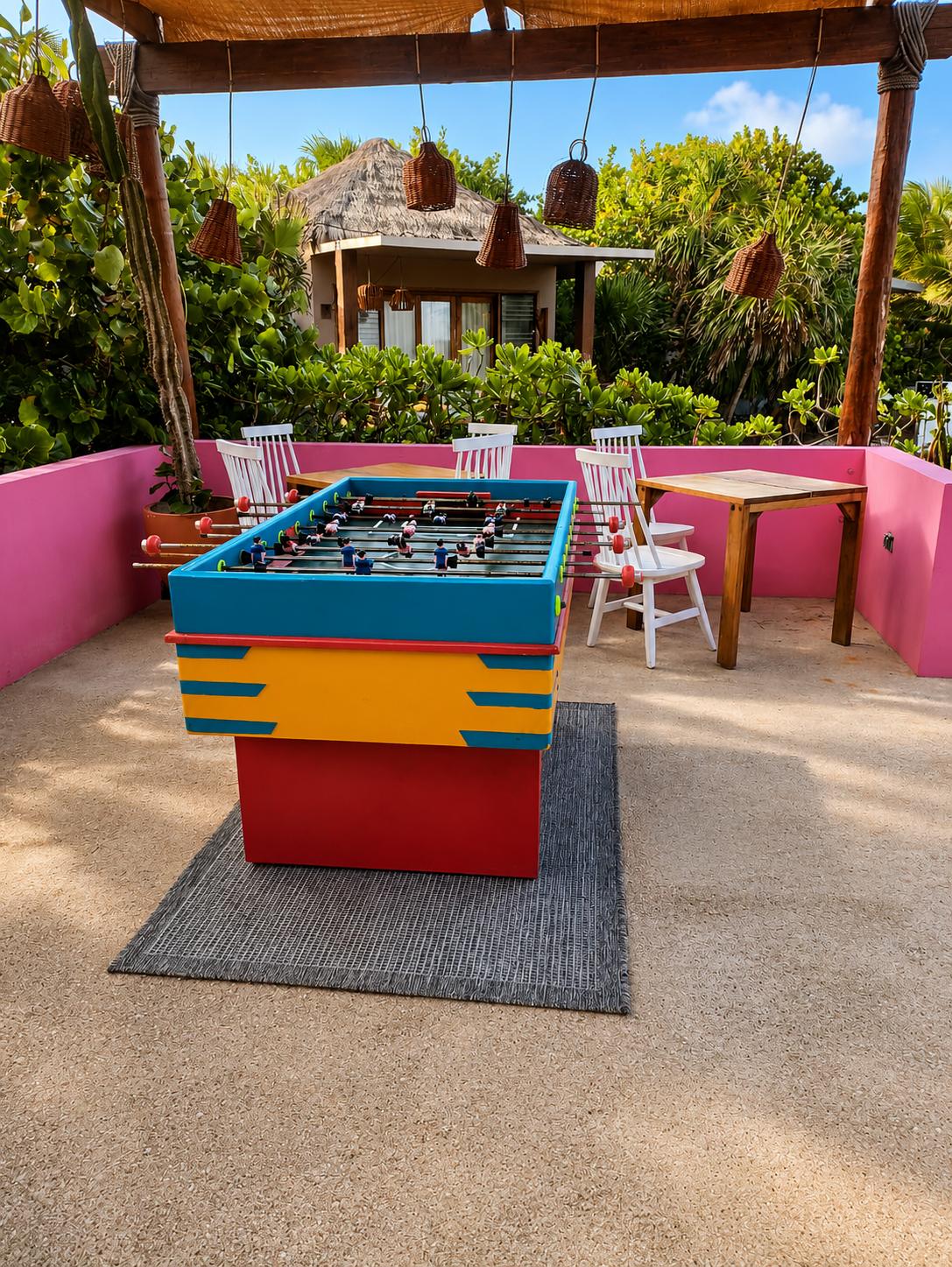 A colorful foosball table sits on a sunny, pink-walled outdoor terrace surrounded by tropical greenery at La Zebra.