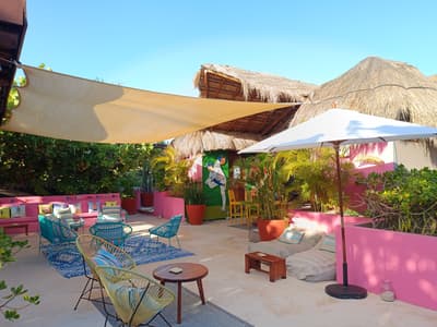 Blue chairs and floor cushions sit on the sunny outdoor patio at La Zebra under shade sails and thatched roofs.