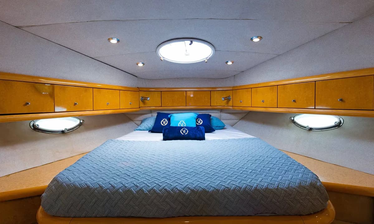 Cozy yacht cabin with a double bed, wood storage cabinets, portholes, and a skylight.