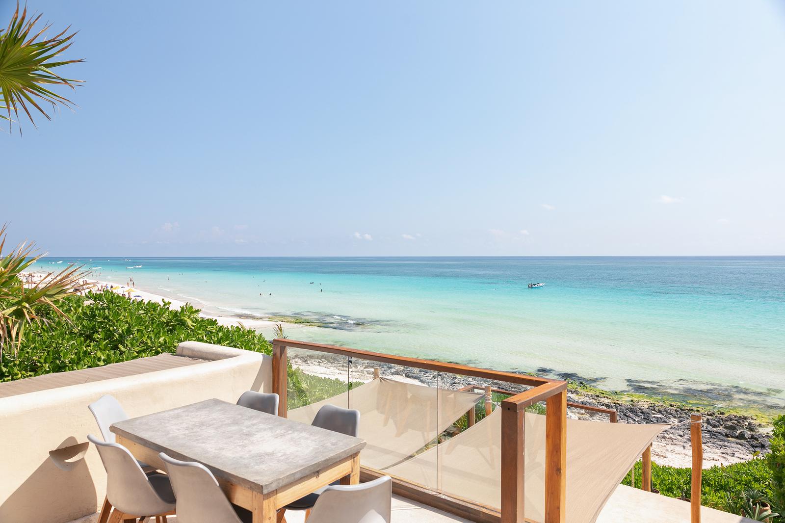 Mezzanine terrace with dining table overlooking turquoise Caribbean waters and white sand beach in Tulum