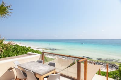 Mezzanine terrace with dining table overlooking turquoise Caribbean waters and white sand beach in Tulum