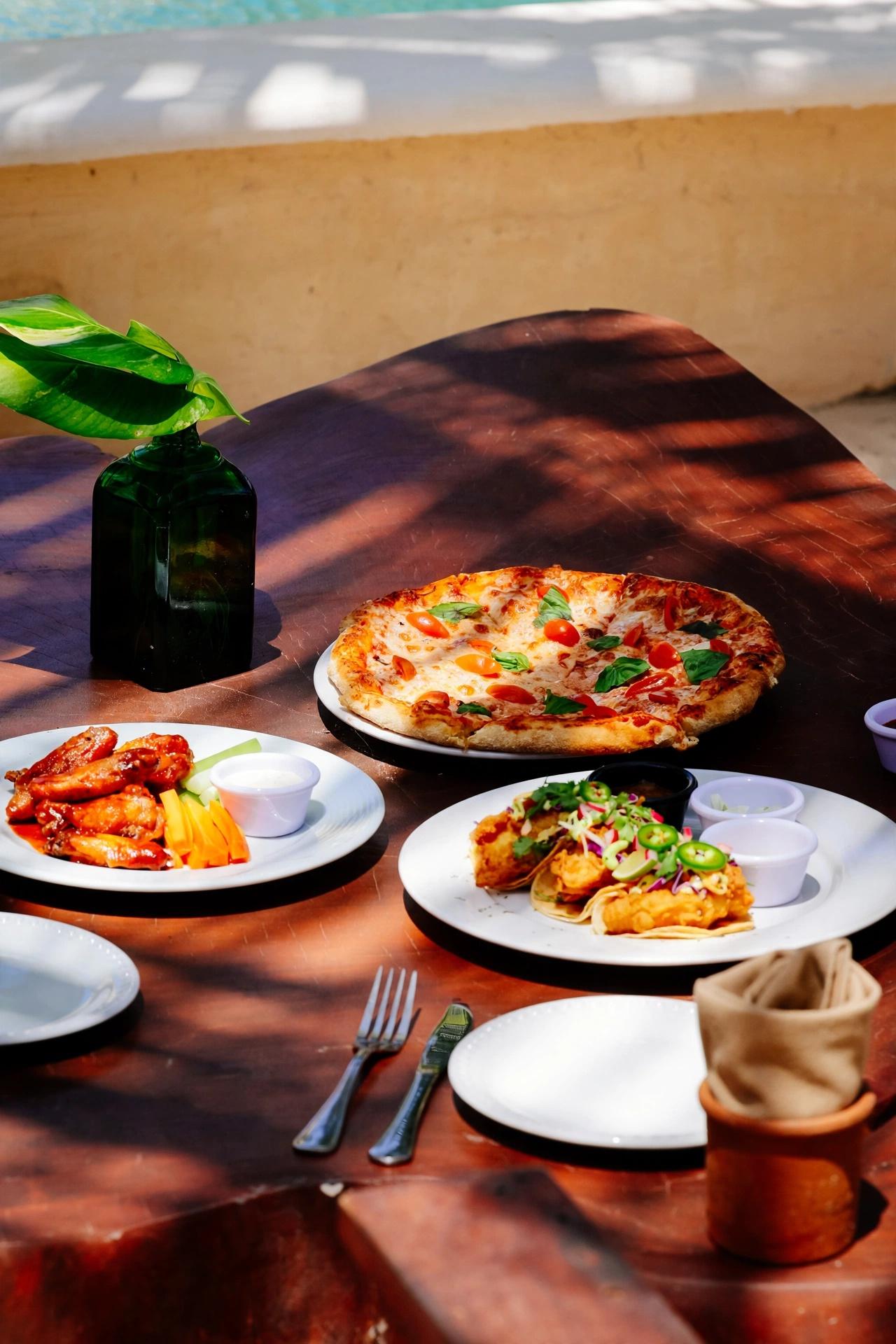 Tulumania table with pizza, chicken wings, tacos, and drinks in warm sunlight.