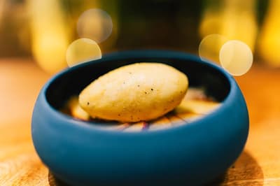 A yellow quenelle of vanilla-speckled sorbet rests over sliced fruit in a dark blue bowl under