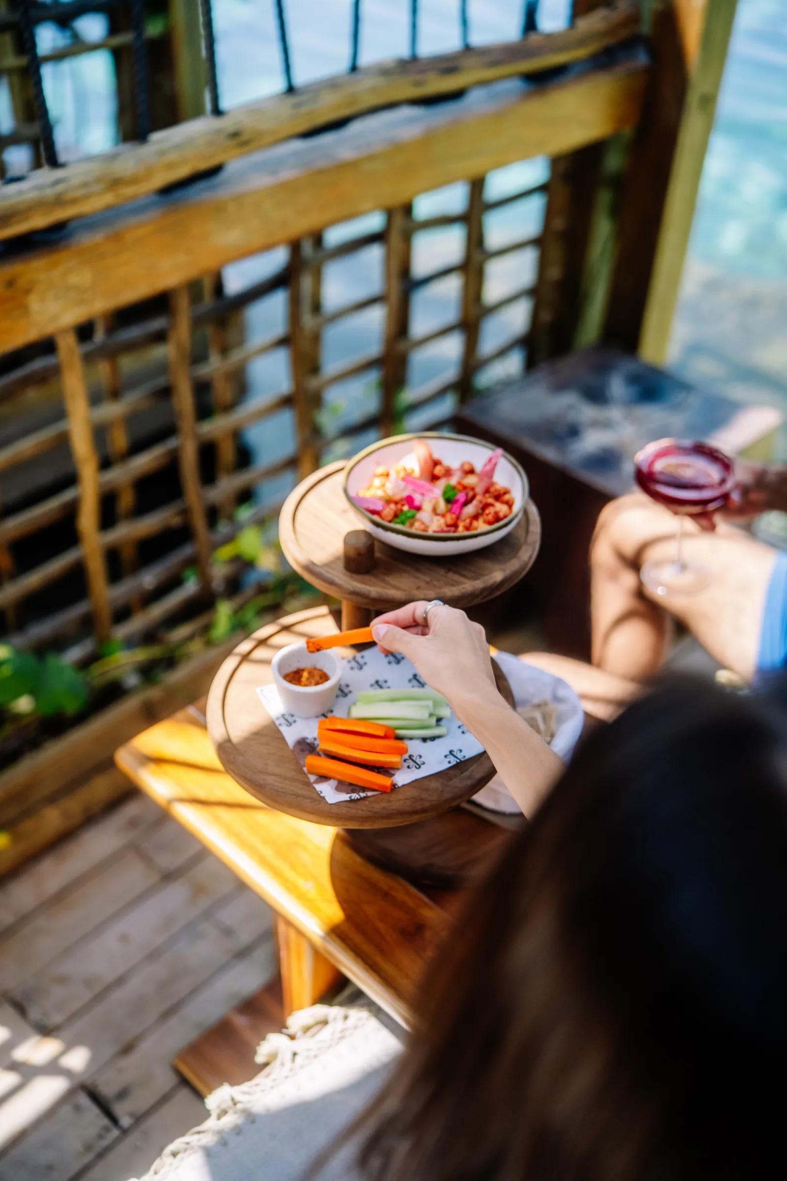 A guest reaches for vegetable sticks served on a tiered wooden tray on Atta's sunny, relaxed