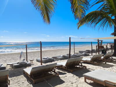 Sun loungers sit on the white sand beach facing a clear blue ocean at La Zebra Mediterranean in Tulum.