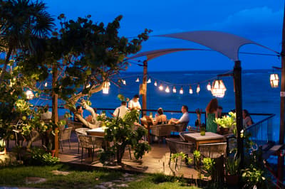 Mezzanine terrace at dusk with diners seated at tables under sail shade structures and hanging lanterns overlooking the