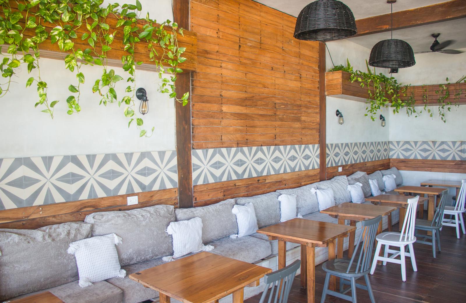 La Zebra Mediterranean dining room with wooden beams, geometric tile accents, gray banquette seating, and wooden tables with