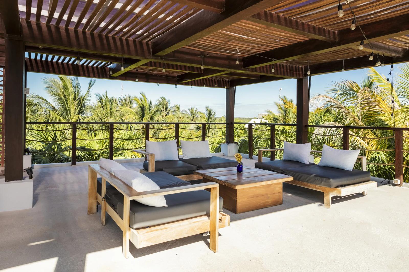 La Zebra Mediterranean's covered terrace with wooden lounge seating, palm trees, and ocean views in Tulum.