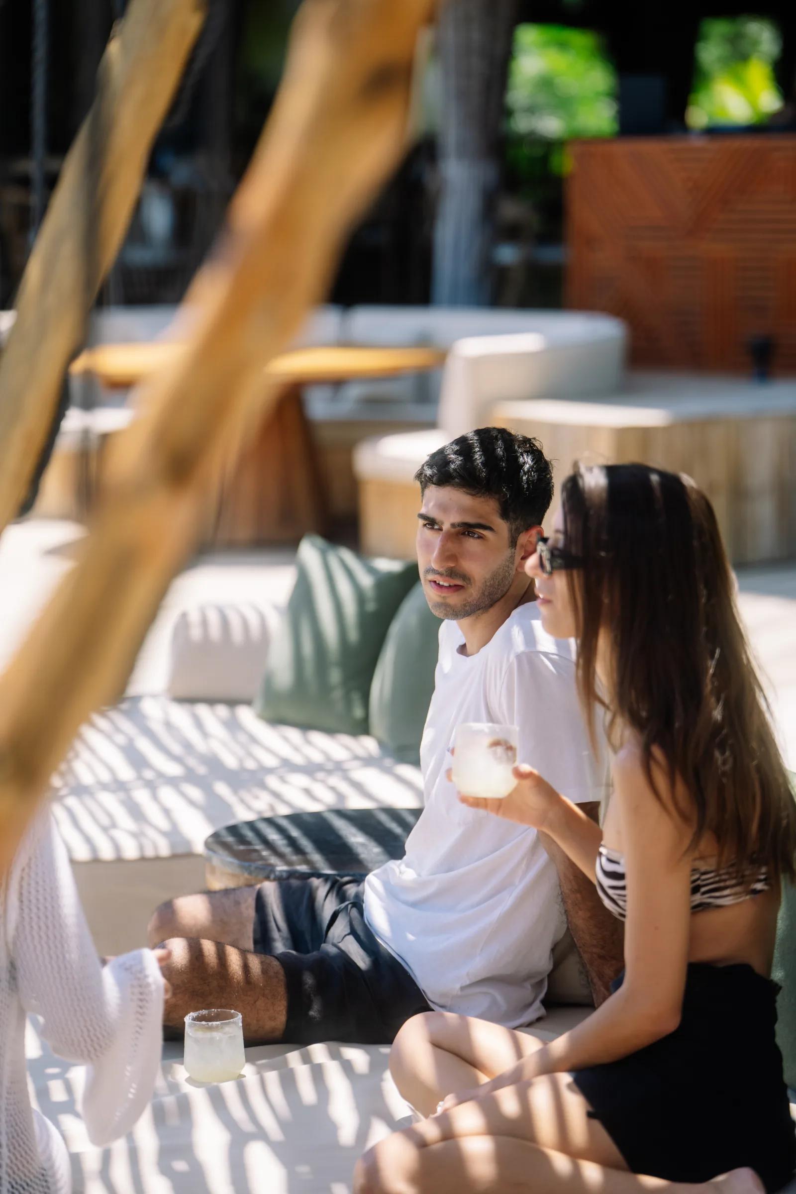 A young couple relaxes with drinks on a shaded outdoor lounge sofa at Atta / Tuuch.