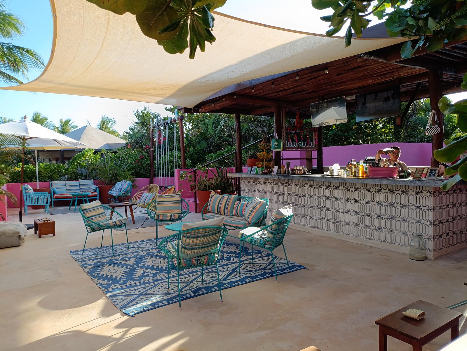 Colorful lounge chairs and a tiled bar stand under a shade sail on La Zebra's sunny open-air patio.