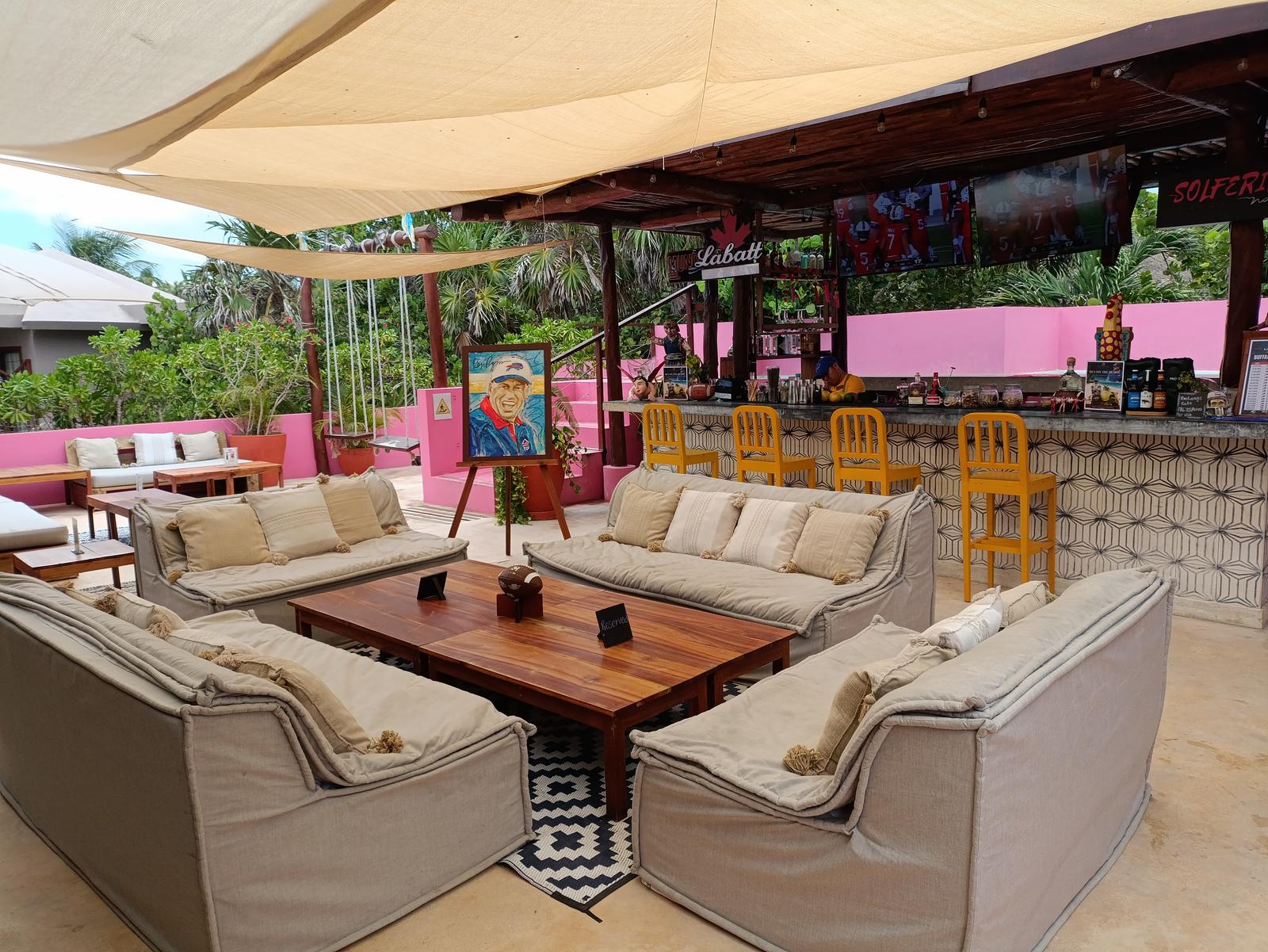 Shaded cushioned sofas surround a wooden coffee table in the relaxed open-air lounge and bar at
