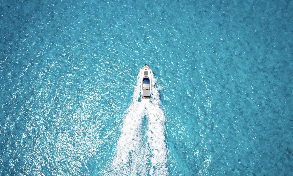 A motor yacht speeds across clear turquoise sea, leaving a white wake in a bright, calm setting.