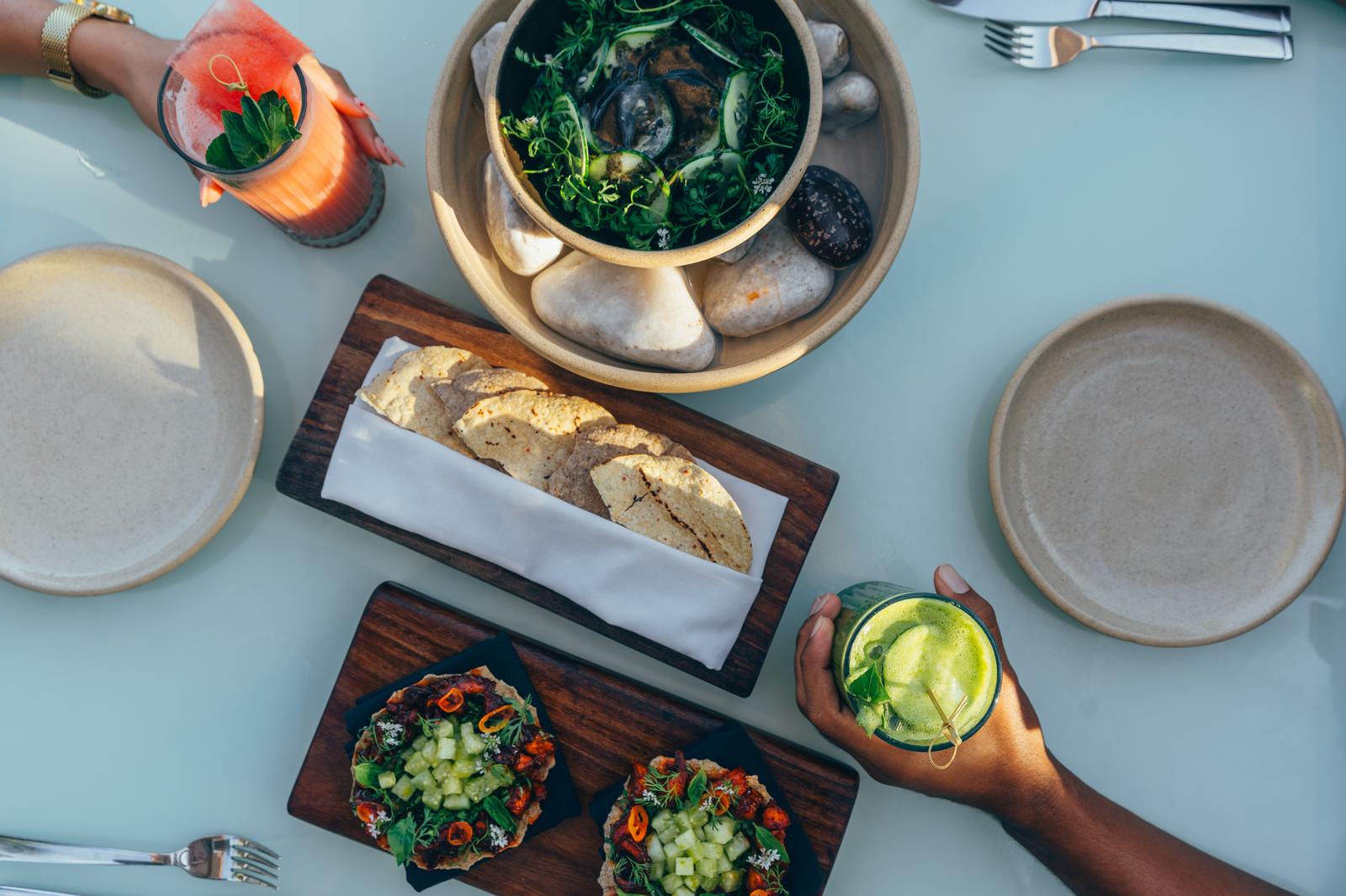 Mi Amor dining table with cocktails, bread, mussels in greens, and appetizers on wooden boards