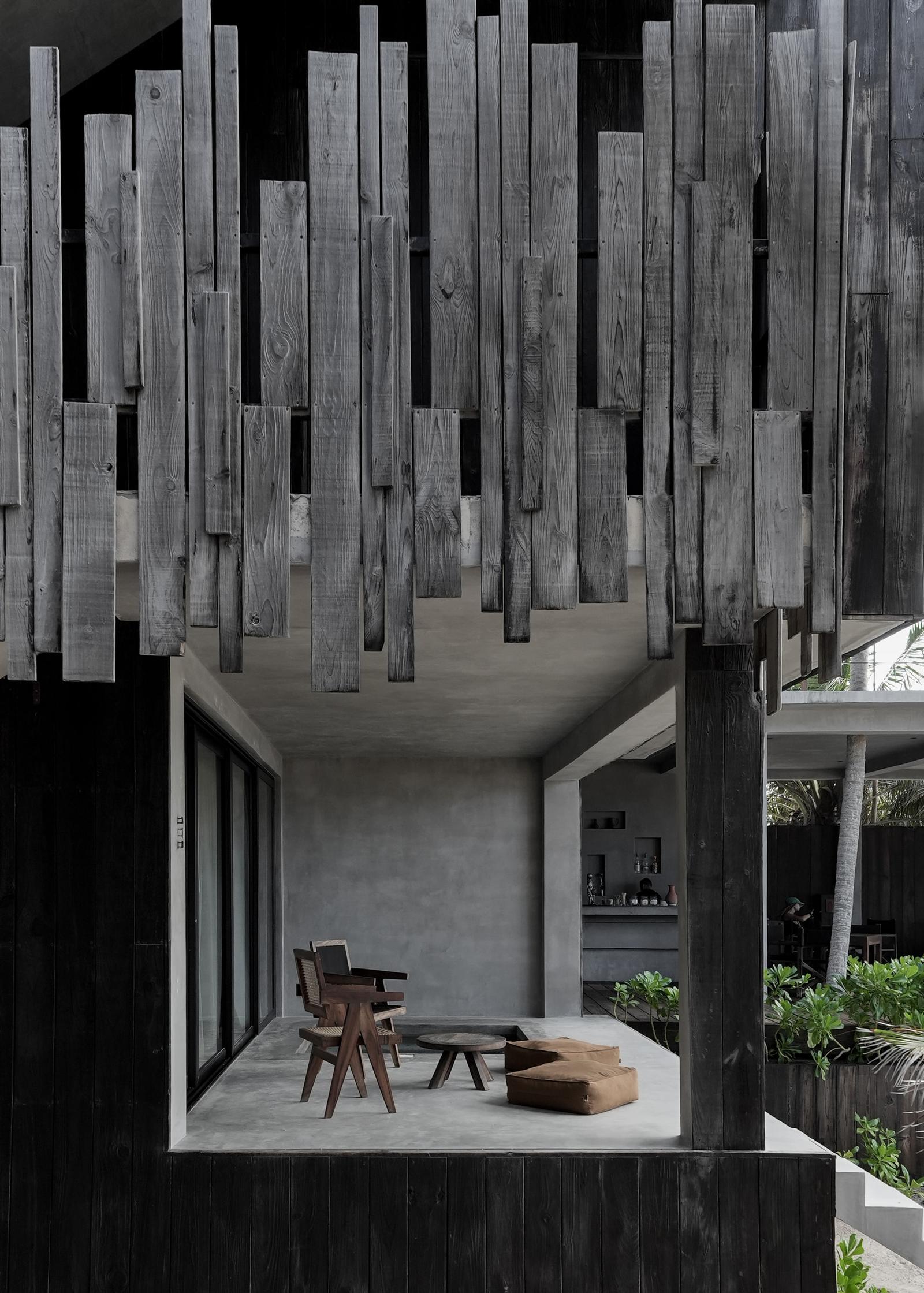 Modern pavilion with weathered wood slat ceiling, concrete interior, wooden chairs, and tropical plants visible at Umi